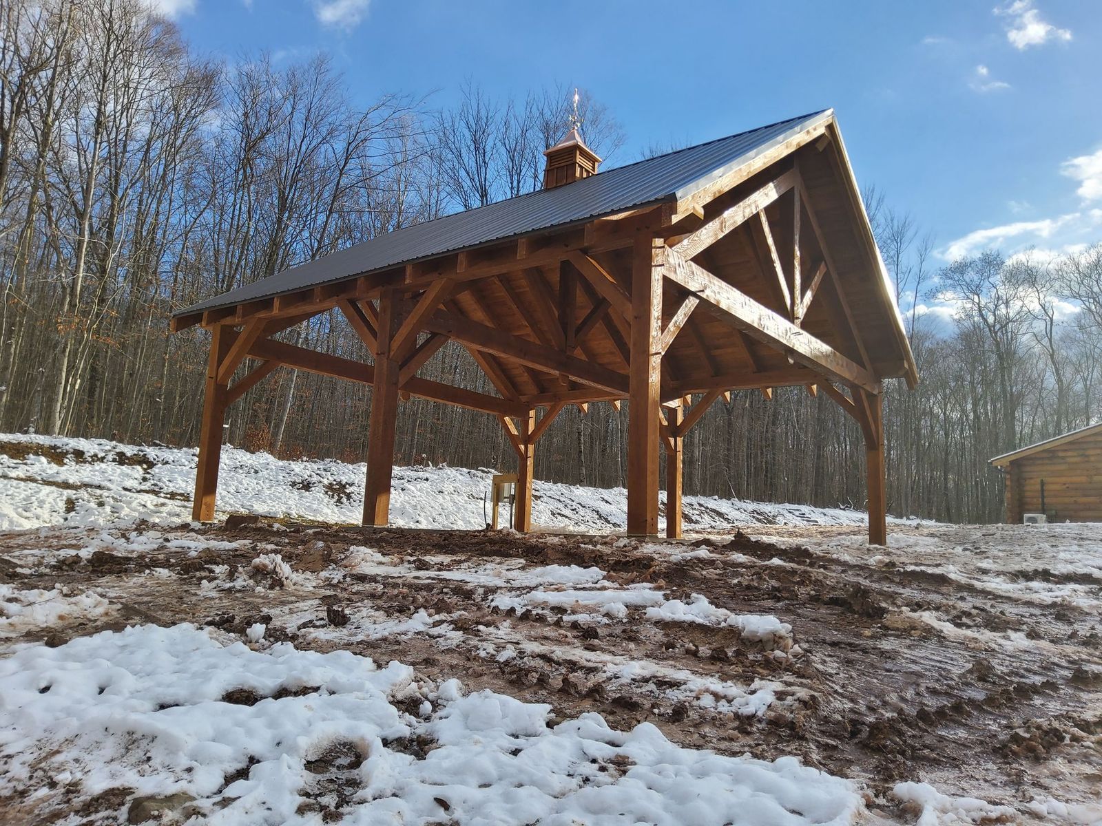 A wooden timber-frame pavilion by Central Timber Frame Supply serving PA, WV, VA, NY, NJ stands in a snowy, muddy field 