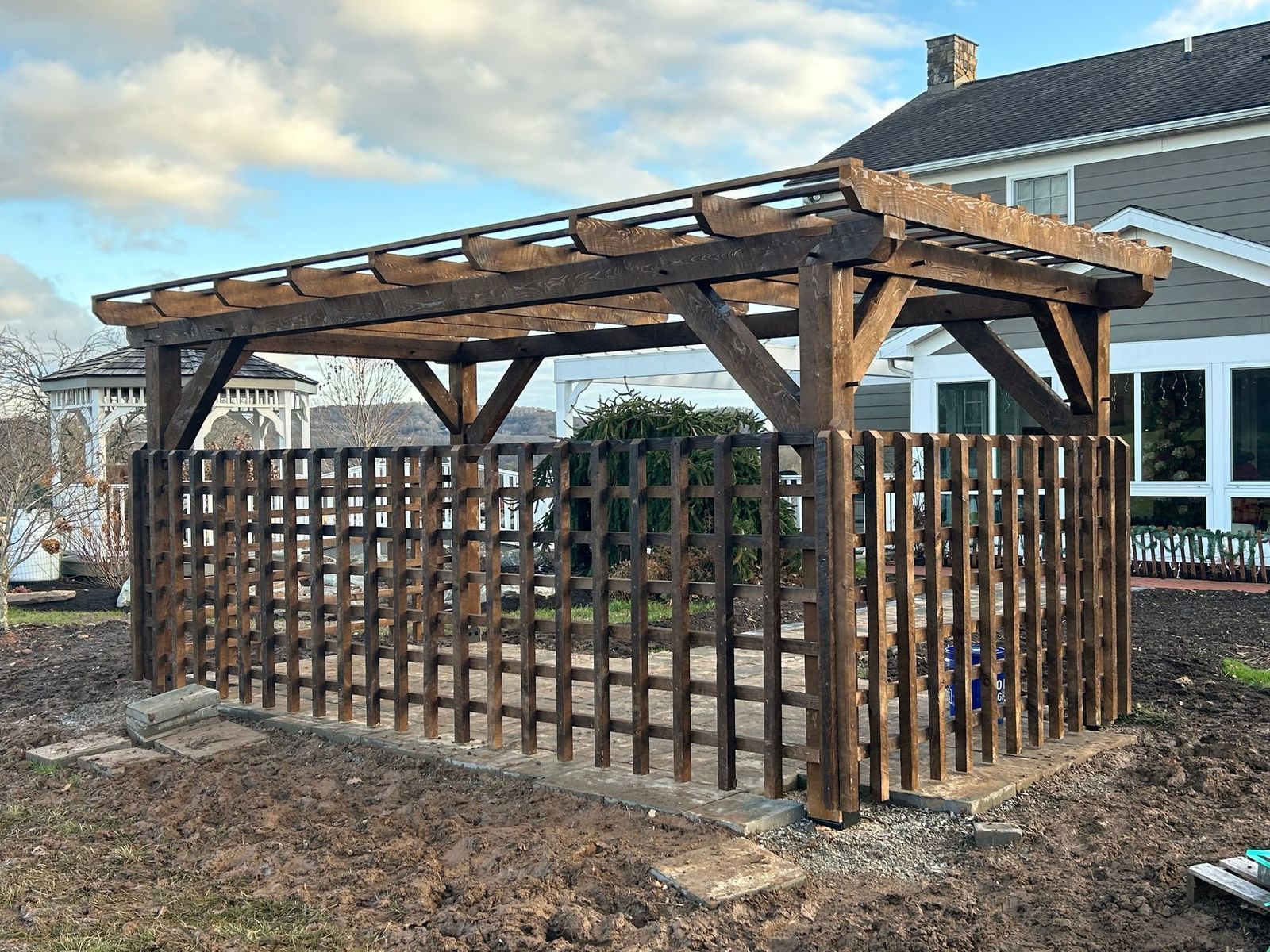A dark wooden pergola by Central Timber Frame Supply serving PA, WV, VA, NY, NJ  with a lattice fence 