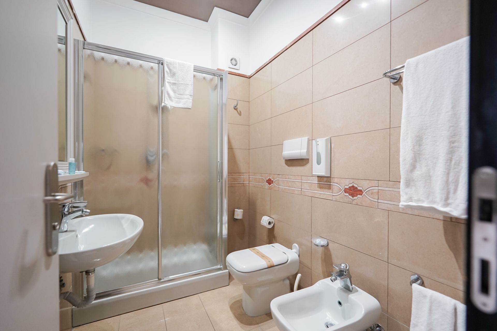Piccolo bagno piastrellato con doccia, lavandino, WC e asciugamani appesi alle pareti.