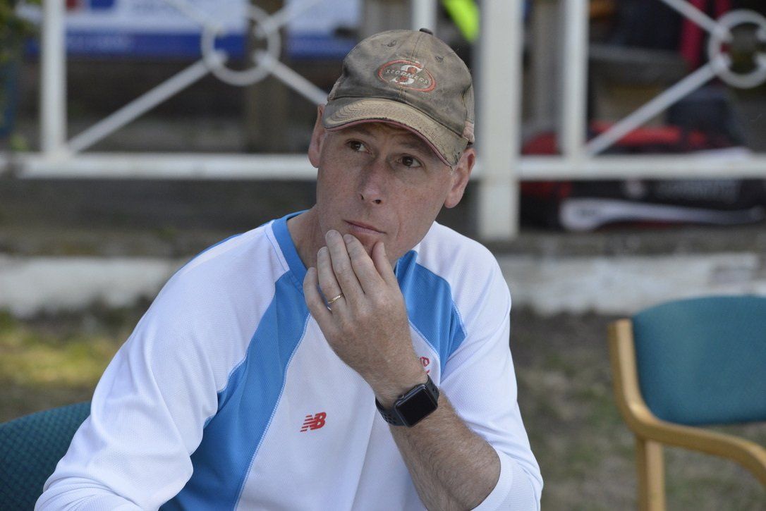 Man in cap and long-sleeve shirt, hand on chin, thoughtful expression. Outdoor setting.