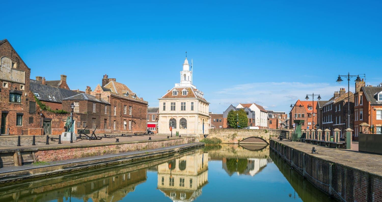 Historic King's Lynn, England, waterfront with buildings, river, bridge, and a white tower under blue sky.