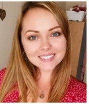 Blonde woman smiles at camera, wearing a red patterned top and necklace.