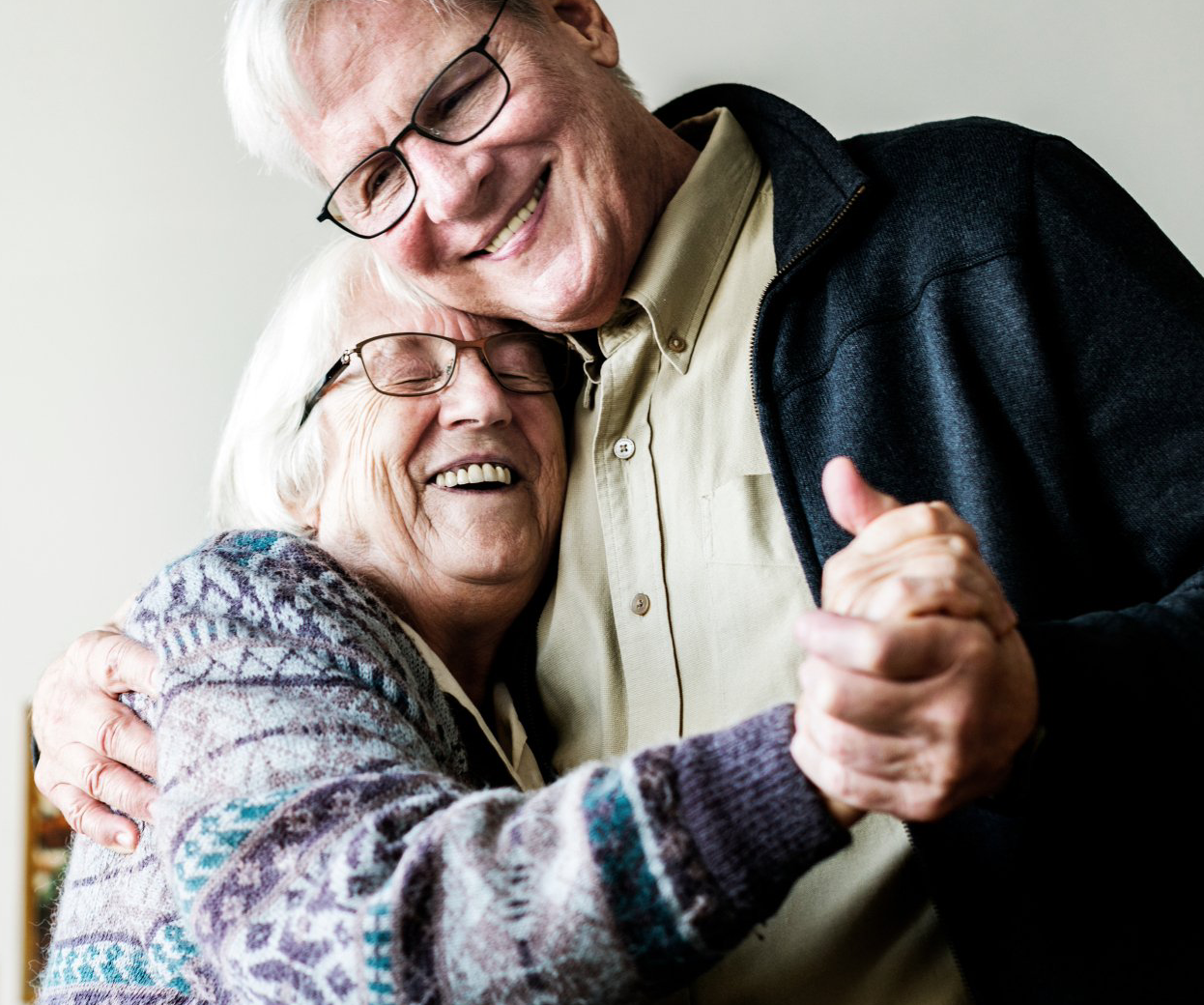 Smiling older couple dancing, indoors. Man in glasses hugs woman.