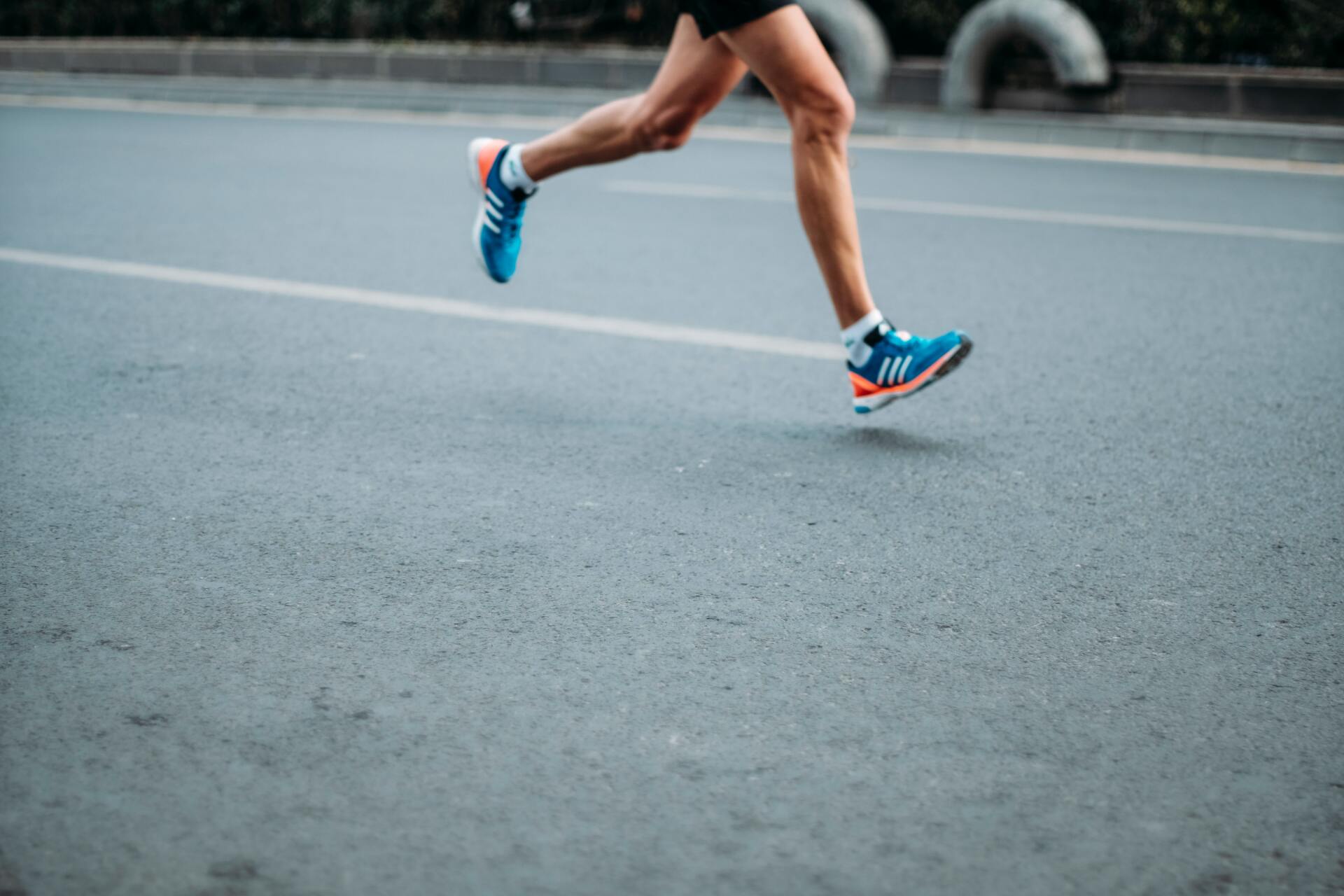 Runner's legs and feet in blue shoes on gray asphalt road.