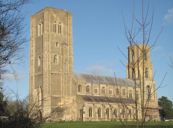 Two large grey stone towers flank a long church with arched windows, against a blue sky.