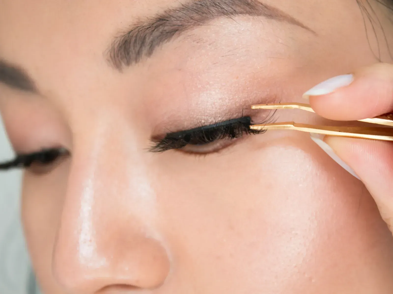 A woman is applying fake eyelashes with tweezers.