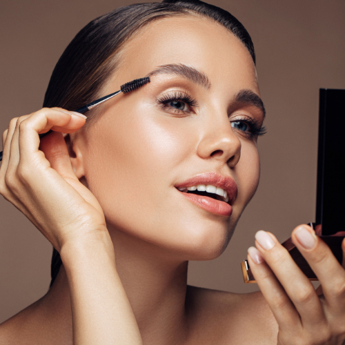 A woman is applying mascara to her eyebrows