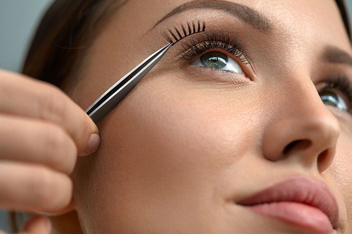 A woman is applying fake eyelashes with tweezers.