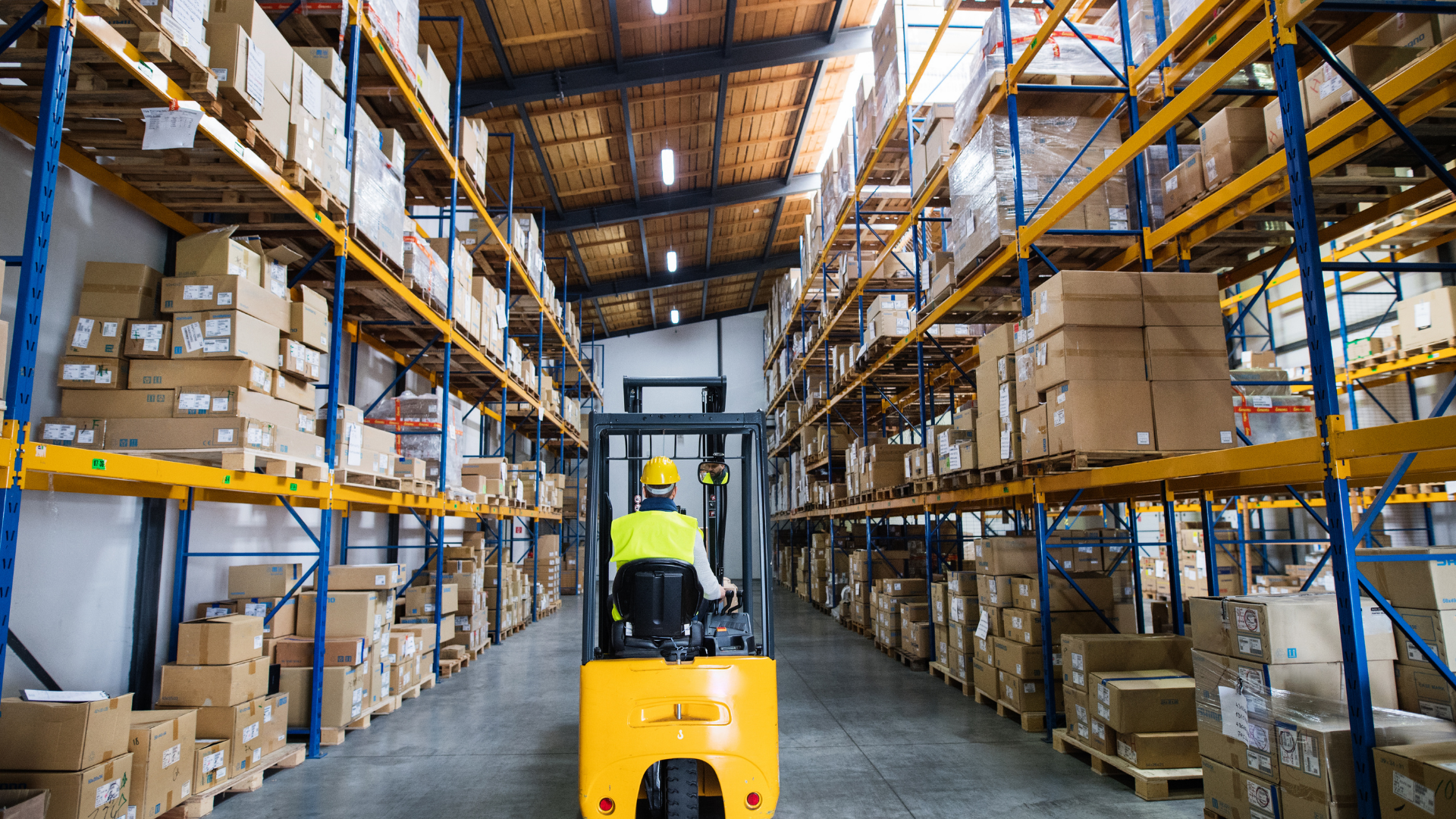 Forklift operator in a warehouse with shelves stacked with boxes.