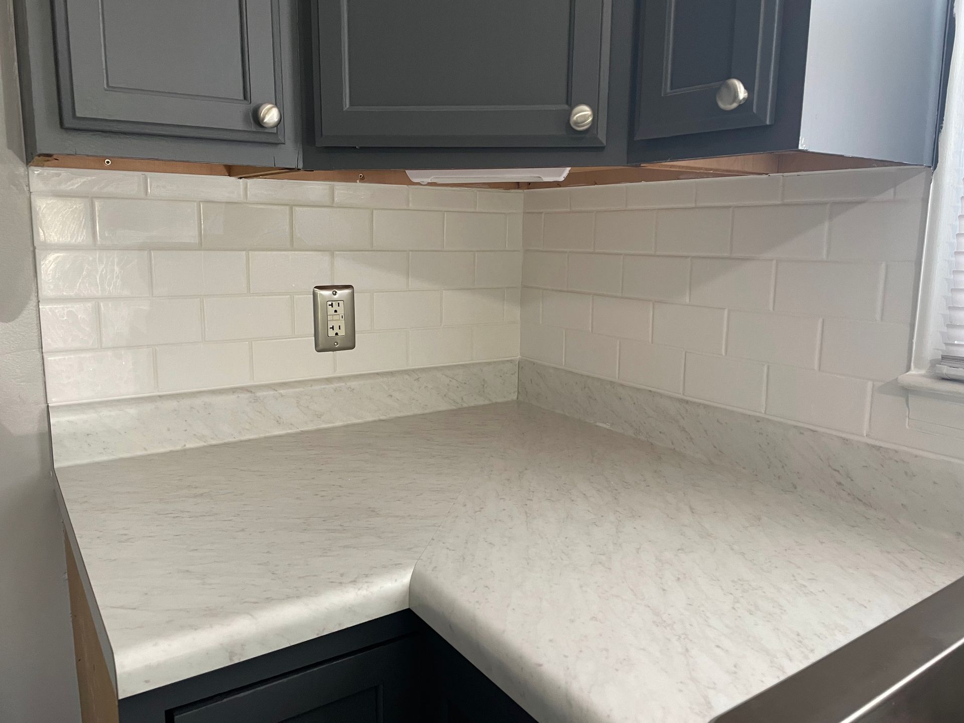 Kitchen corner with white tiled backsplash, gray cabinets, and light-colored countertop.