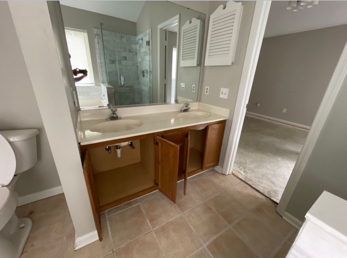 Bathroom with double sink vanity, open cabinet doors, toilet, and neutral colors.