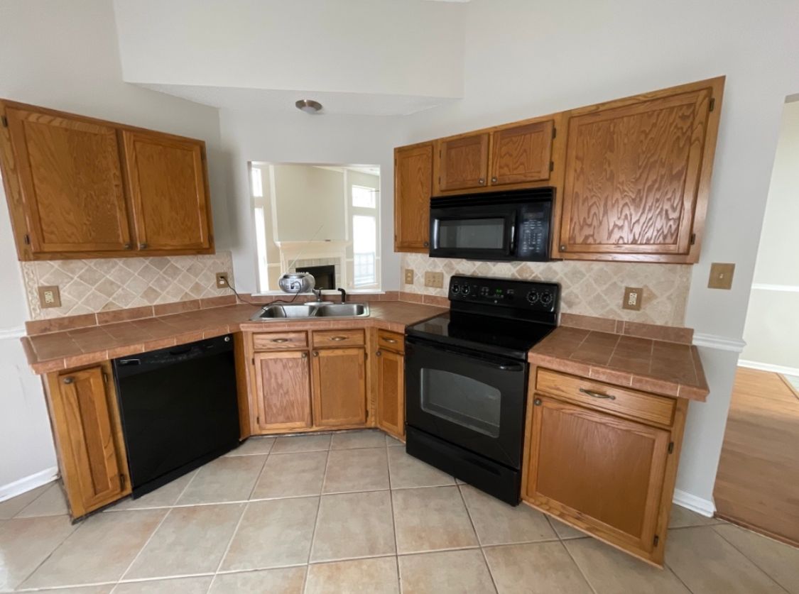 Kitchen with light brown cabinets, black appliances, tile backsplash, and countertops.