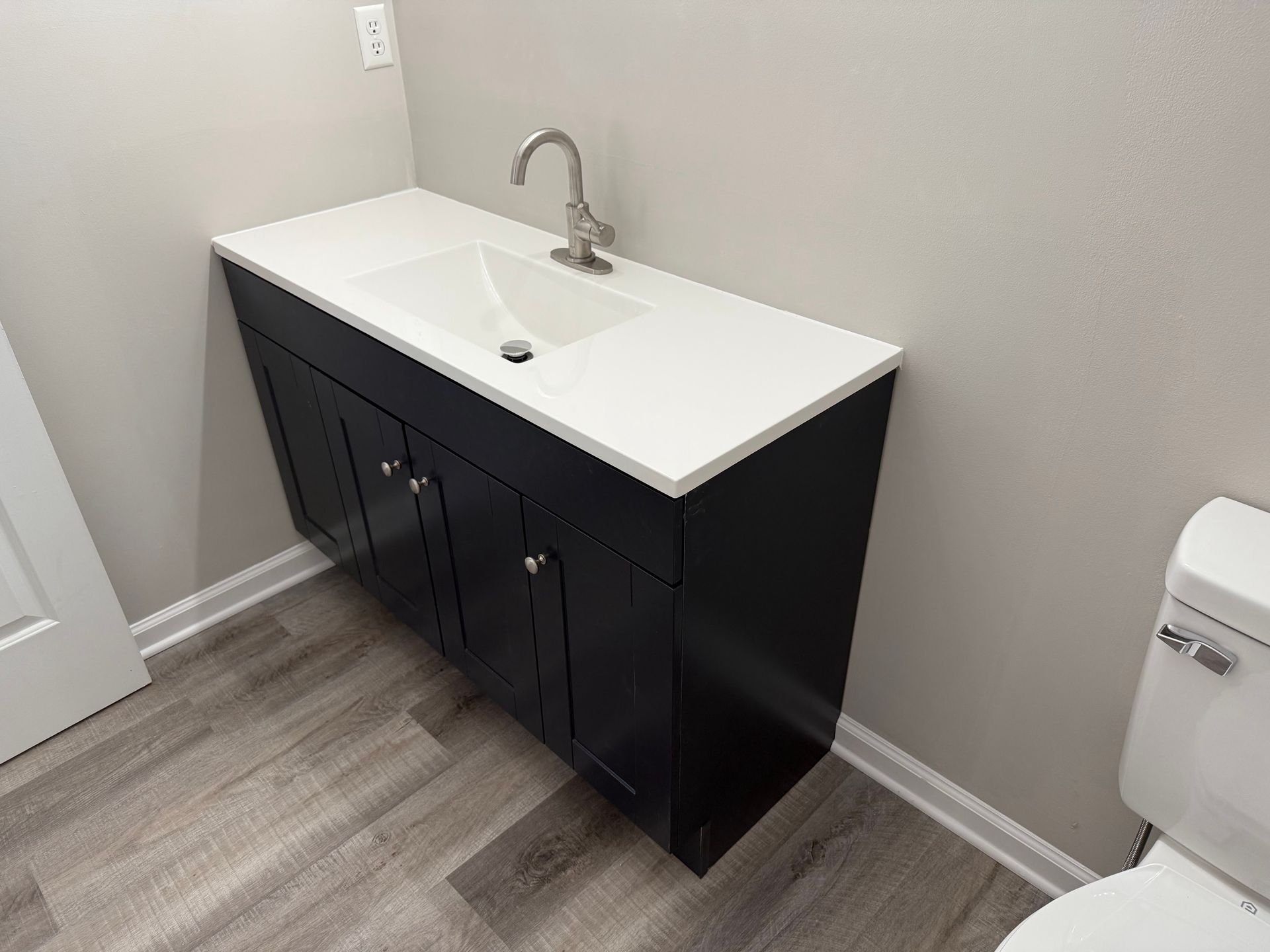 Black bathroom vanity with white countertop and sink against a gray wall, next to a toilet.