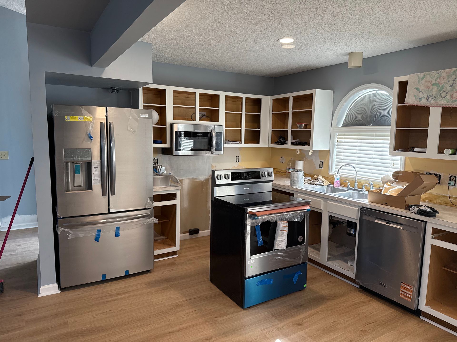 Kitchen undergoing renovation with new appliances, bare cabinets, and light wood flooring.