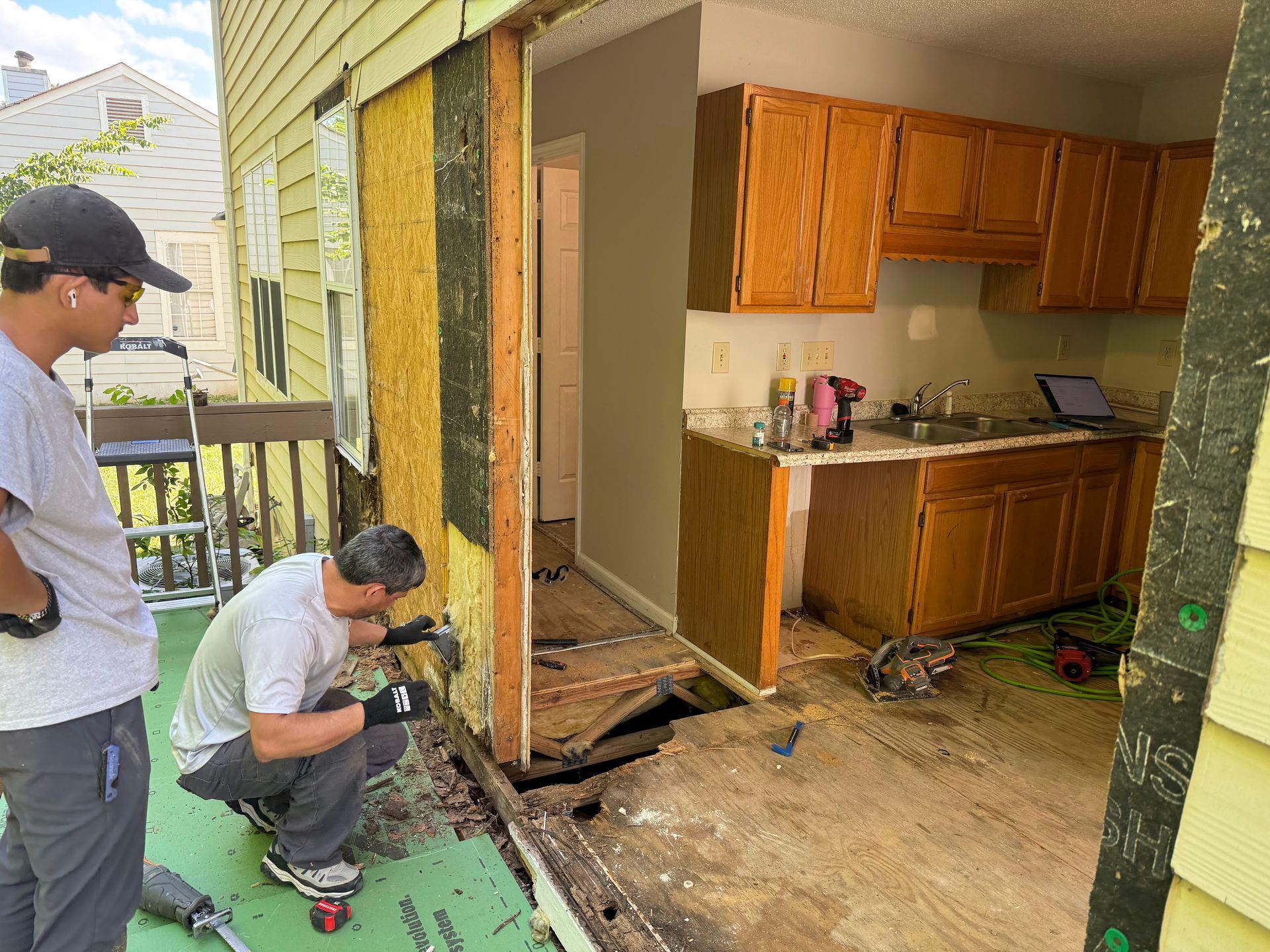 Two workers remove exterior wall to access kitchen.