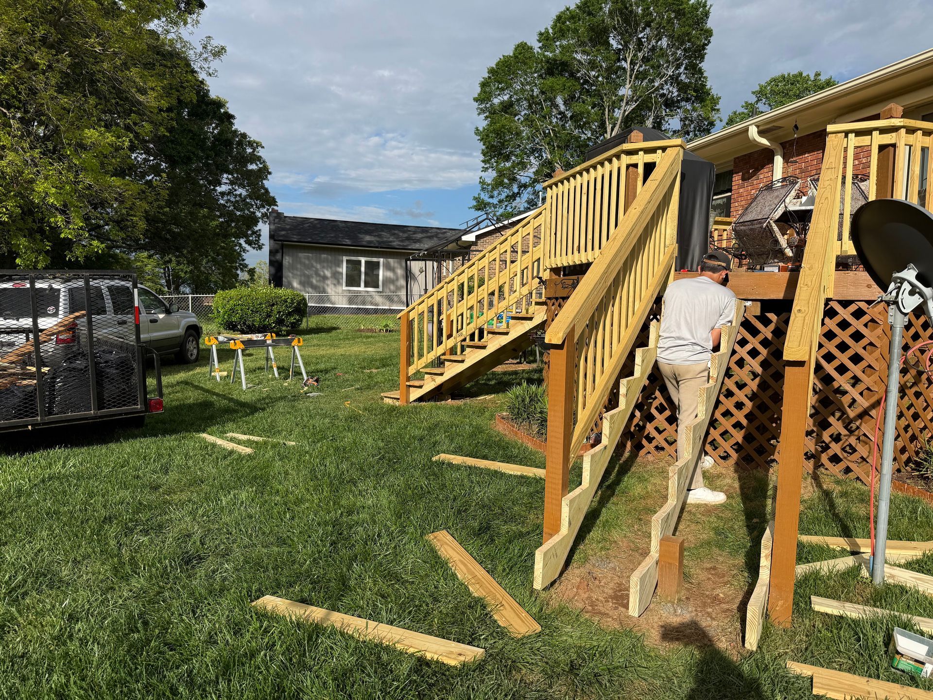 Man building wooden deck stairs in grassy backyard. Bright sunny day.