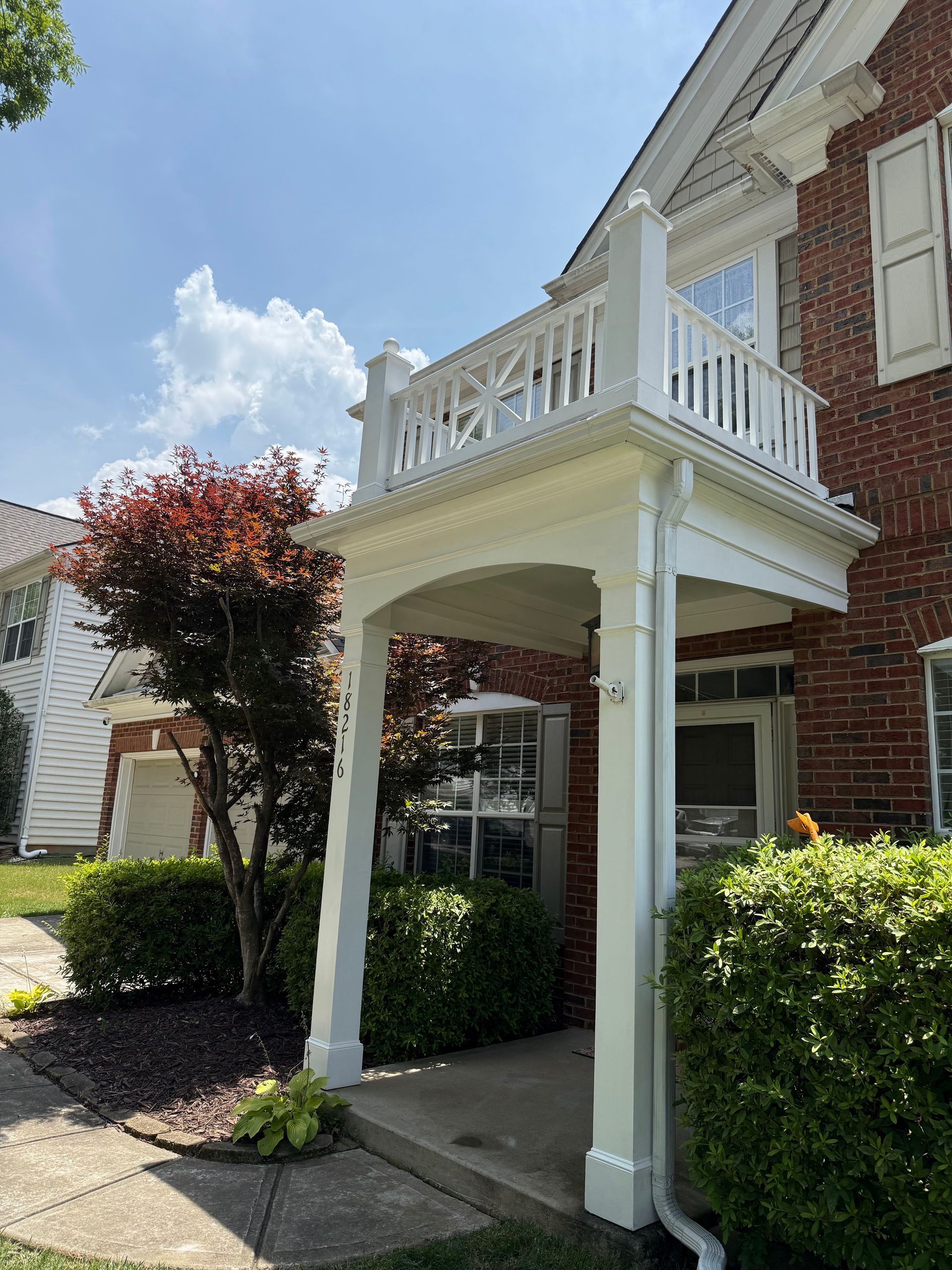 Exterior of a red brick house with a white balcony and porch on a sunny day.