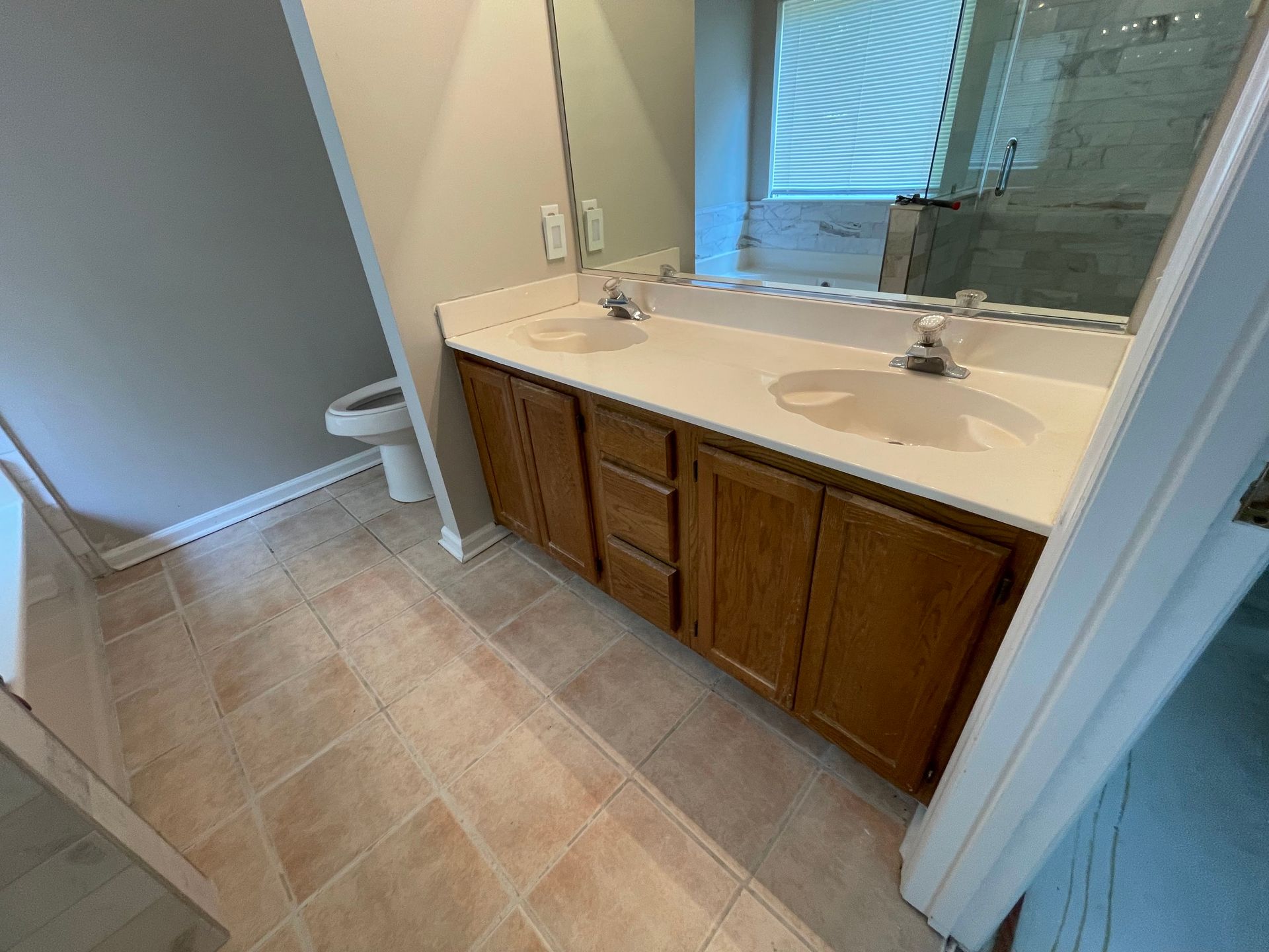 Bathroom with double sink vanity, toilet, tile floor, and shower visible through doorway.