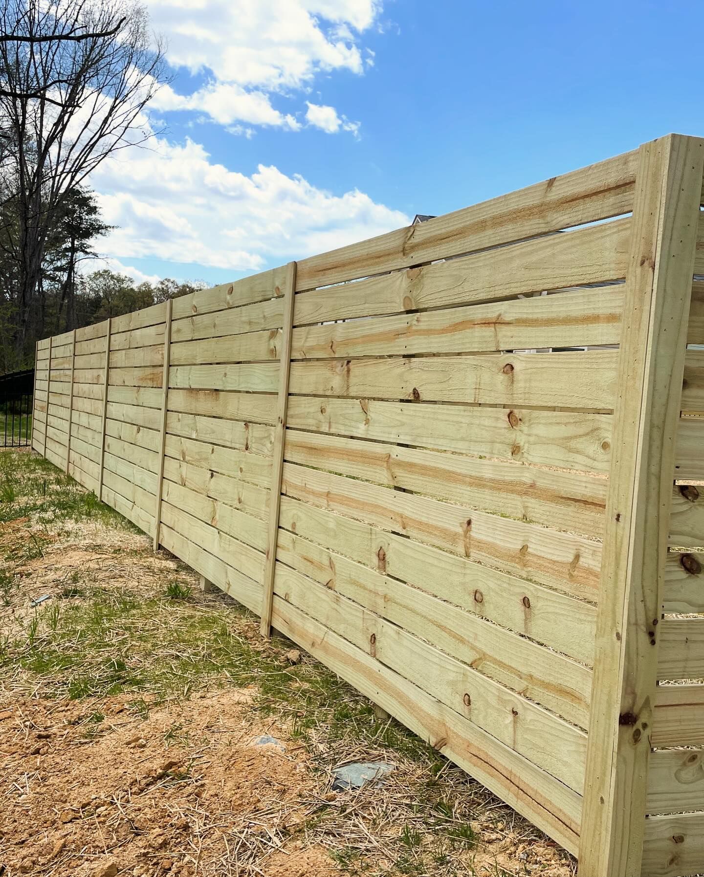 Wooden fence in a grassy yard under a partly cloudy blue sky.