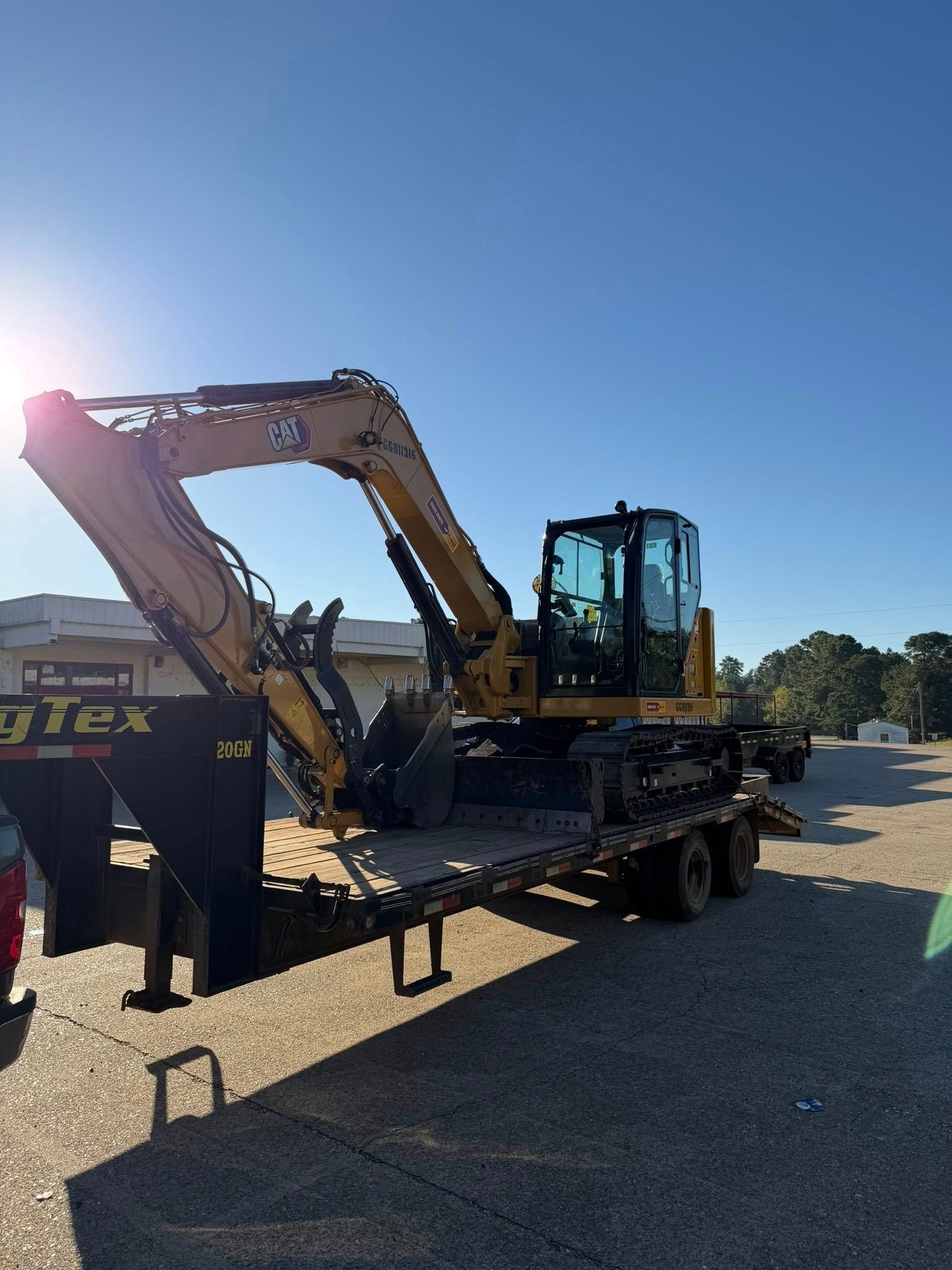 Yellow excavator on a flatbed trailer on a gravel lot under a clear blue sky.
