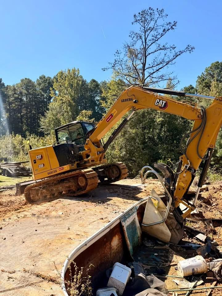 A yellow Caterpillar excavator demolishes a concrete structure under a bright blue sky.