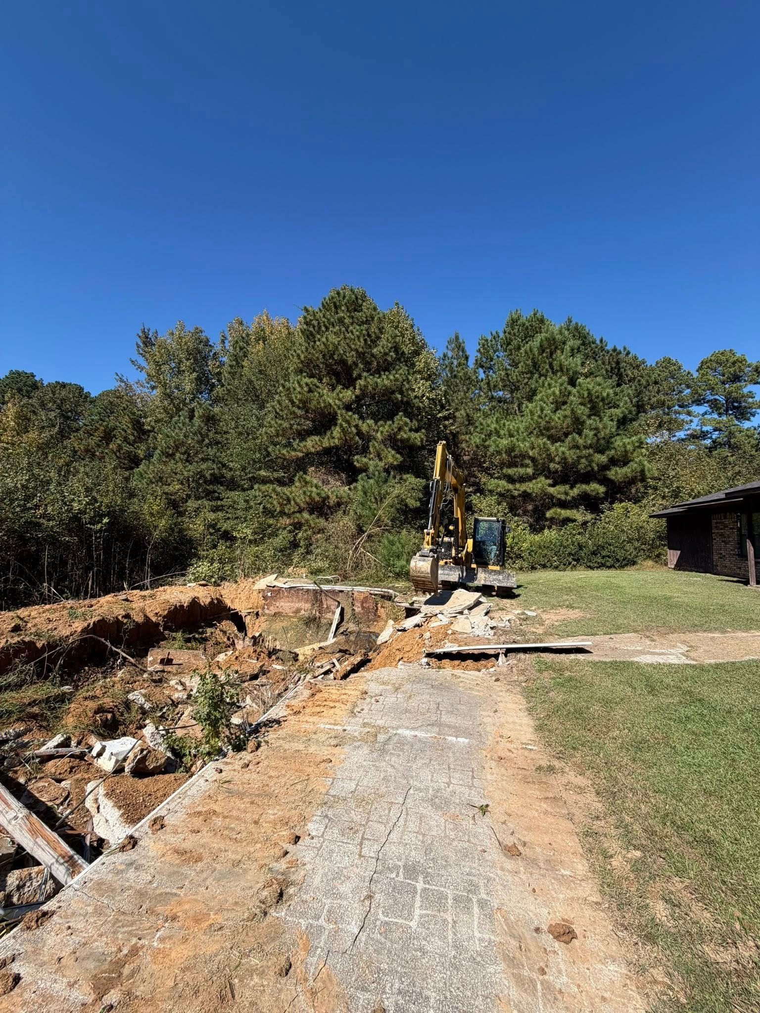 Excavator on a construction site with a concrete path, trees, and blue sky.