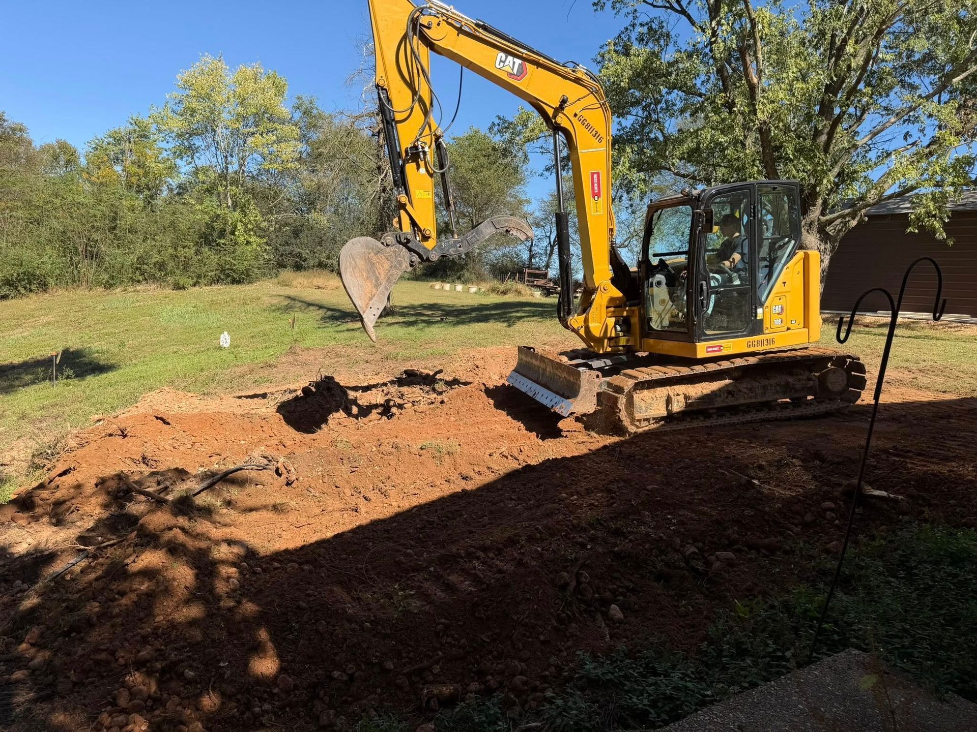 Yellow excavator digging in a grassy yard on a sunny day.