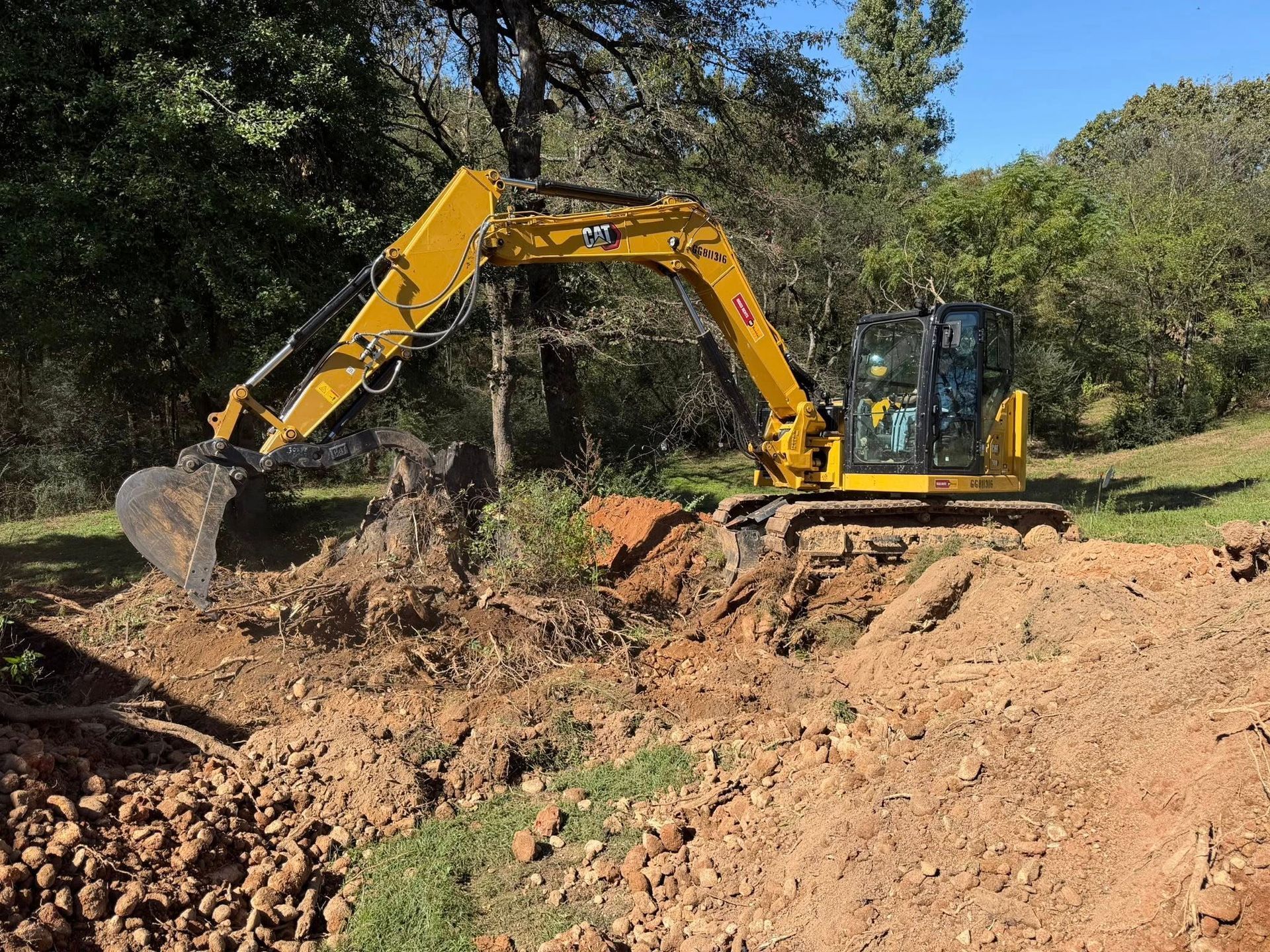 Yellow excavator digging in a dirt area, with a forested background.