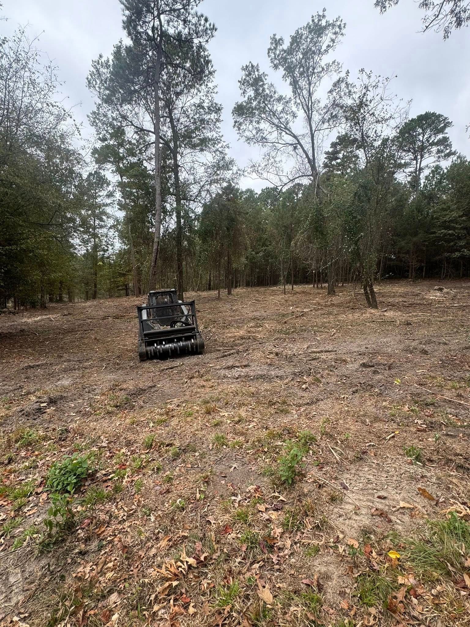 A camouflage ATV sits in a clearing with trees and brown foliage under a cloudy sky.