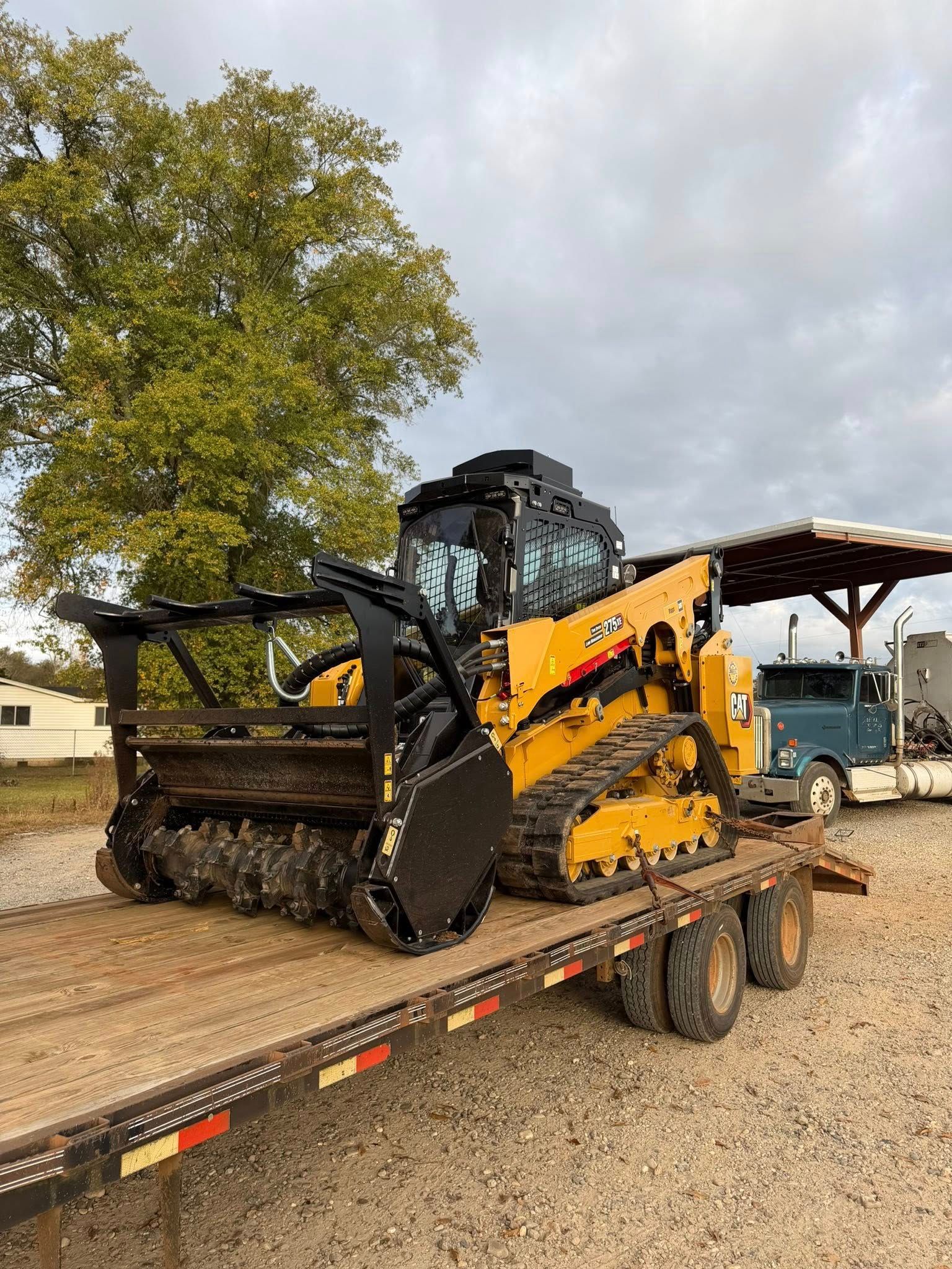 Yellow and black forestry mulcher on a trailer, with a blue truck visible in the background.