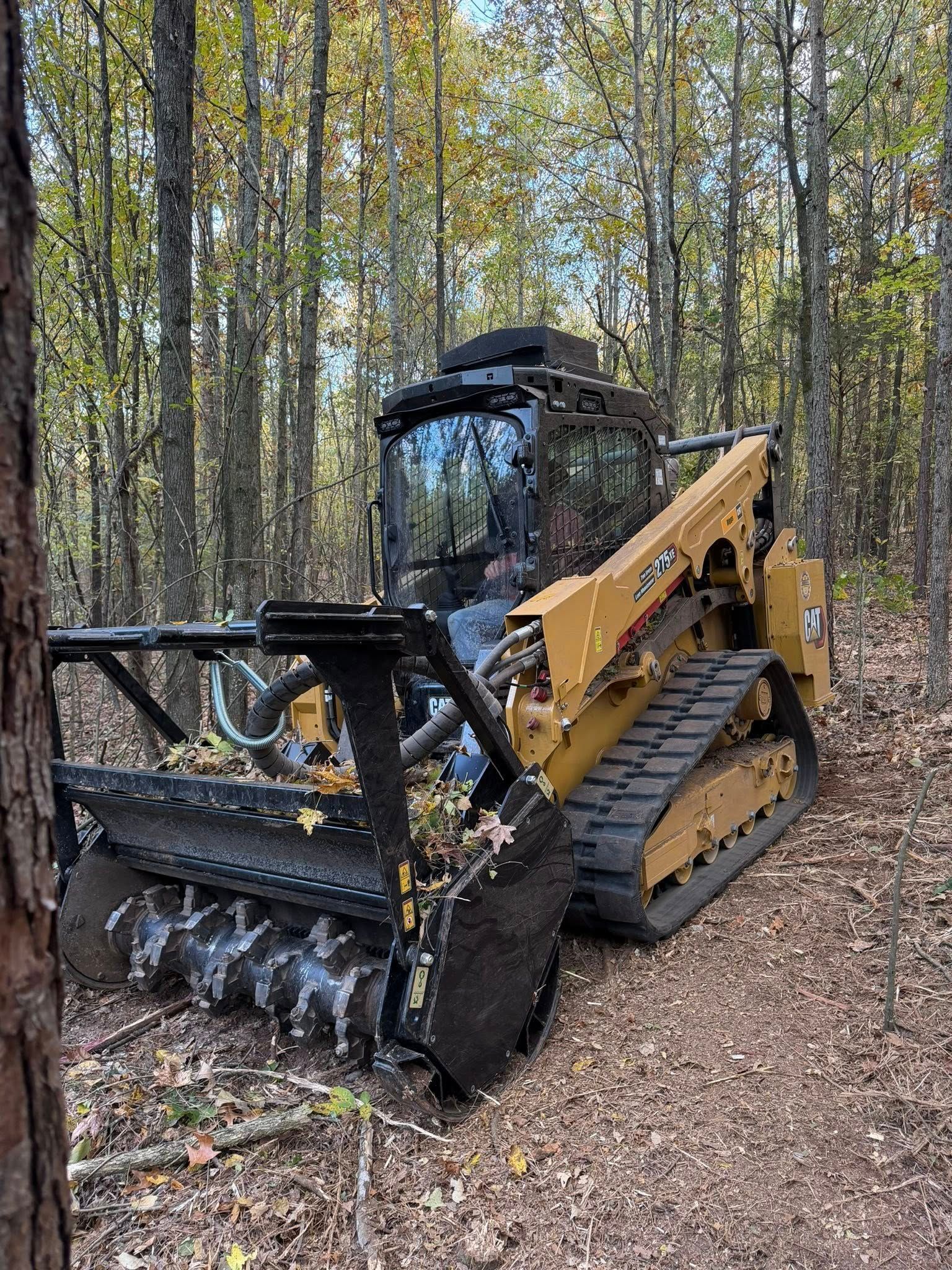 Yellow forestry mulcher clearing a path through a wooded area.