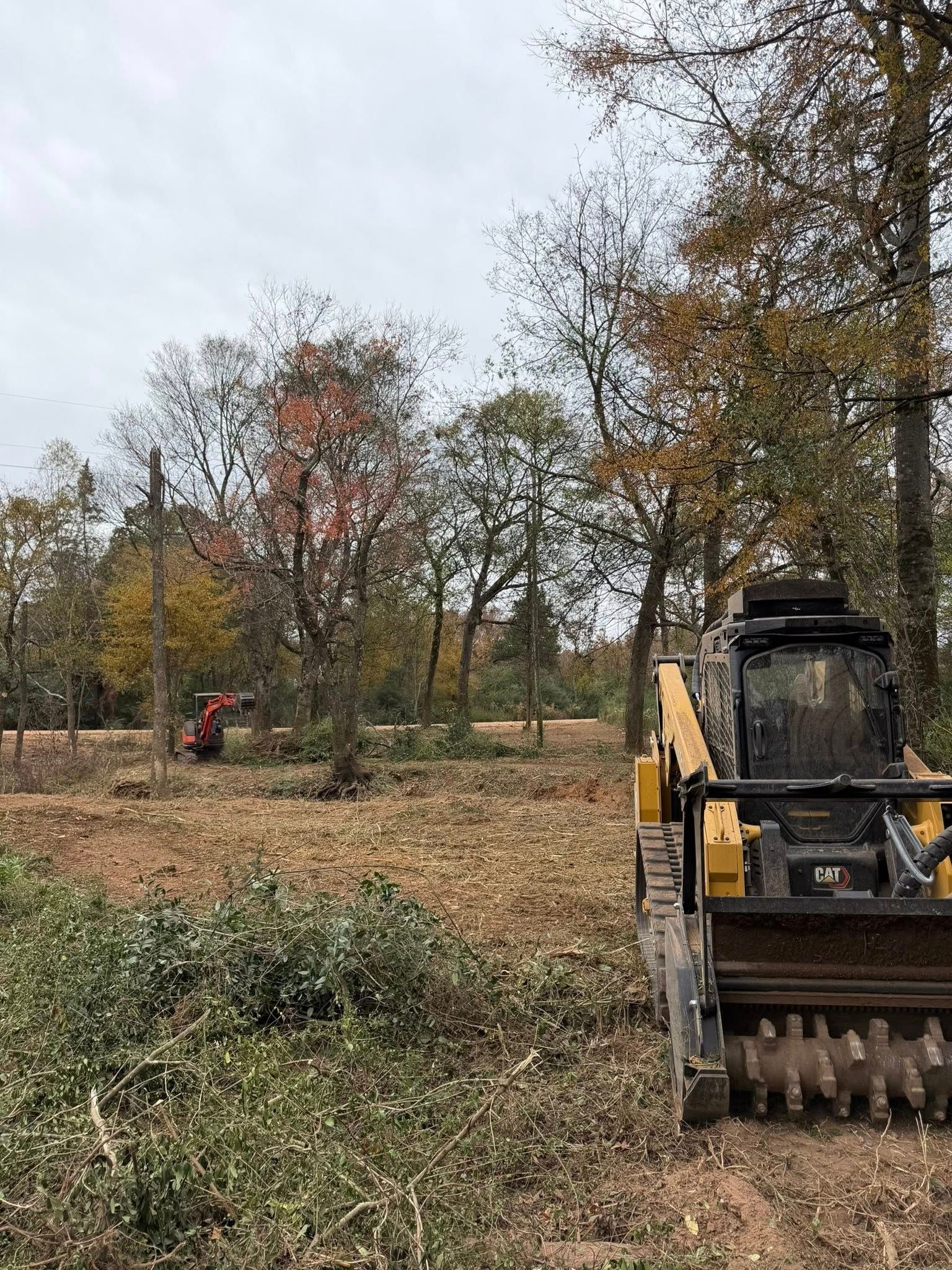 Skid steer mulching a field with trees in the background under an overcast sky.