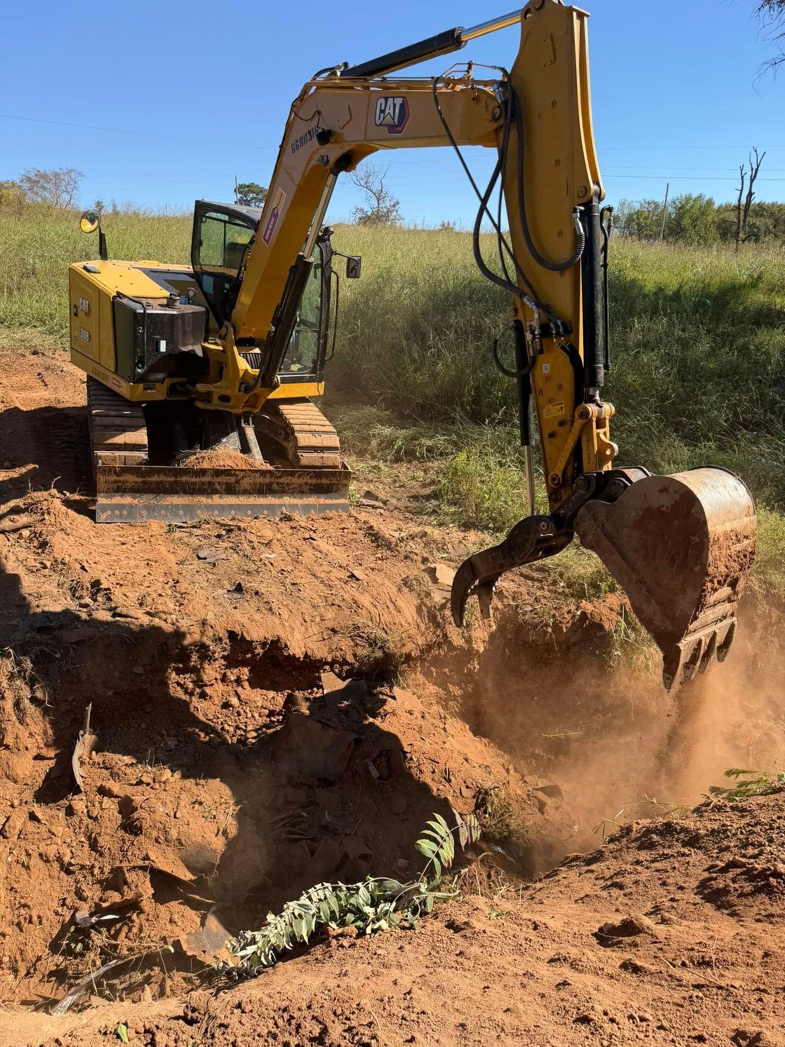 Yellow Caterpillar excavator digging in a dirt pit outdoors on a sunny day.
