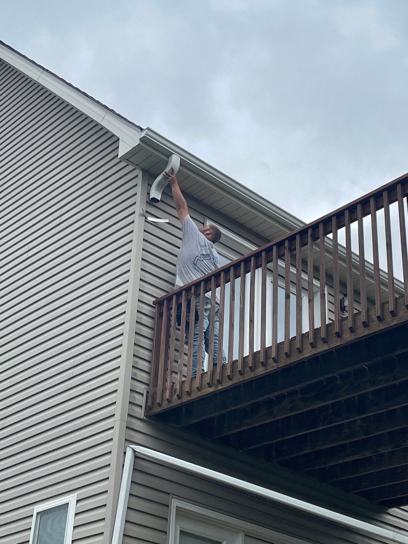 Person painting the eaves of a house from a wooden balcony.