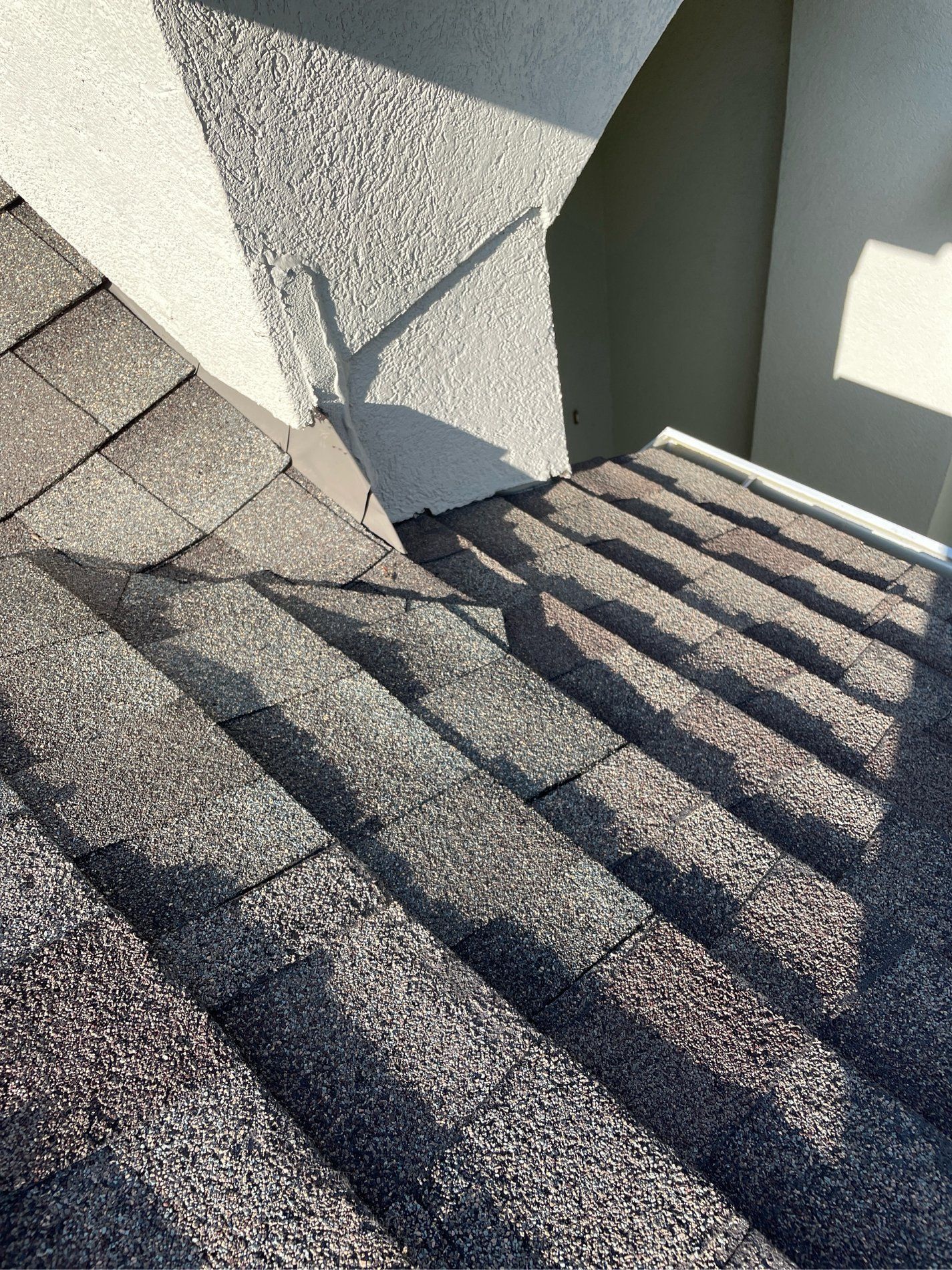 Gloved hand in a red sleeve inspecting a shingled roof seam close-up