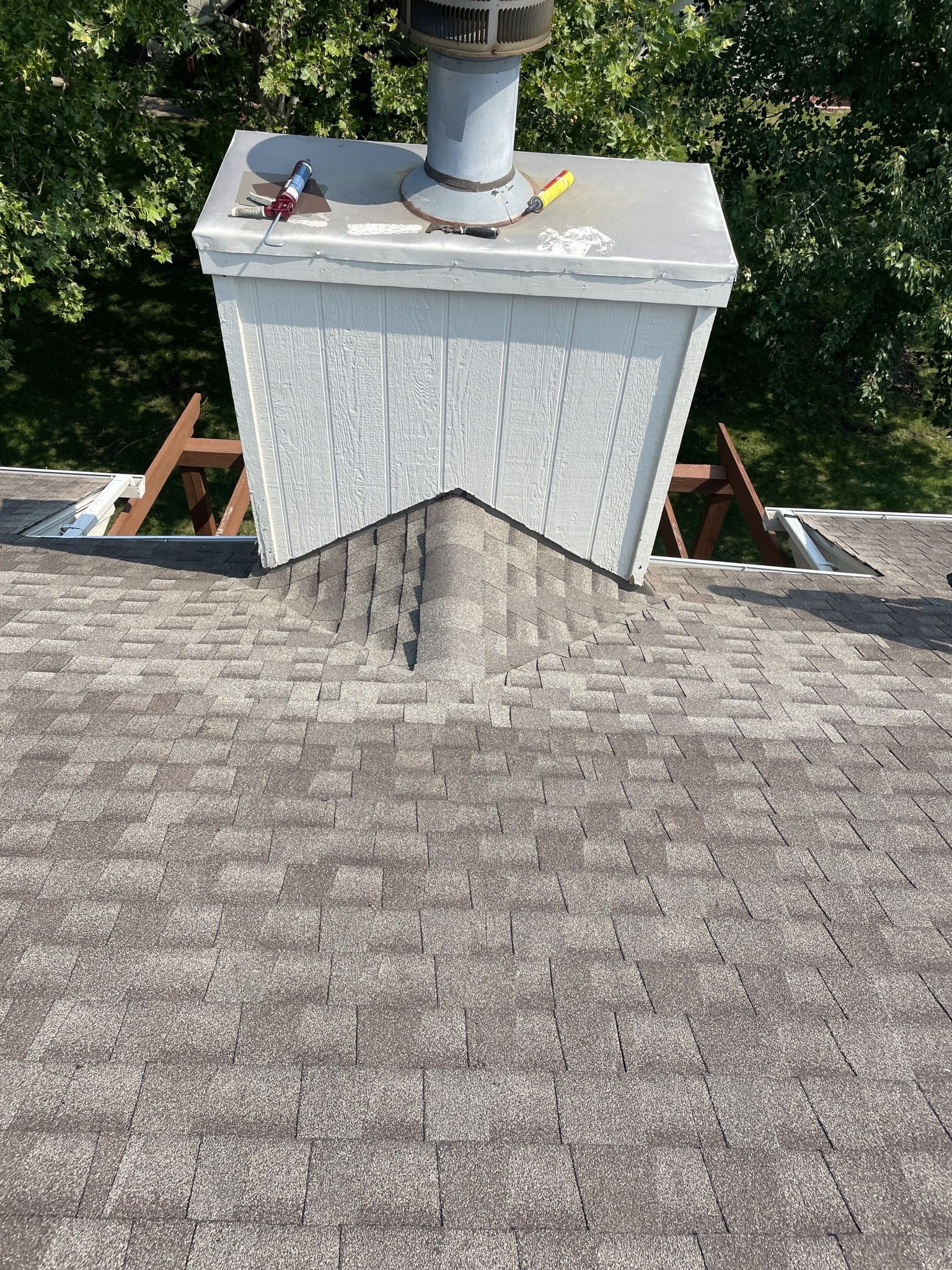 Roofers working on a shingled roof, with a ladder and parked vehicles below.