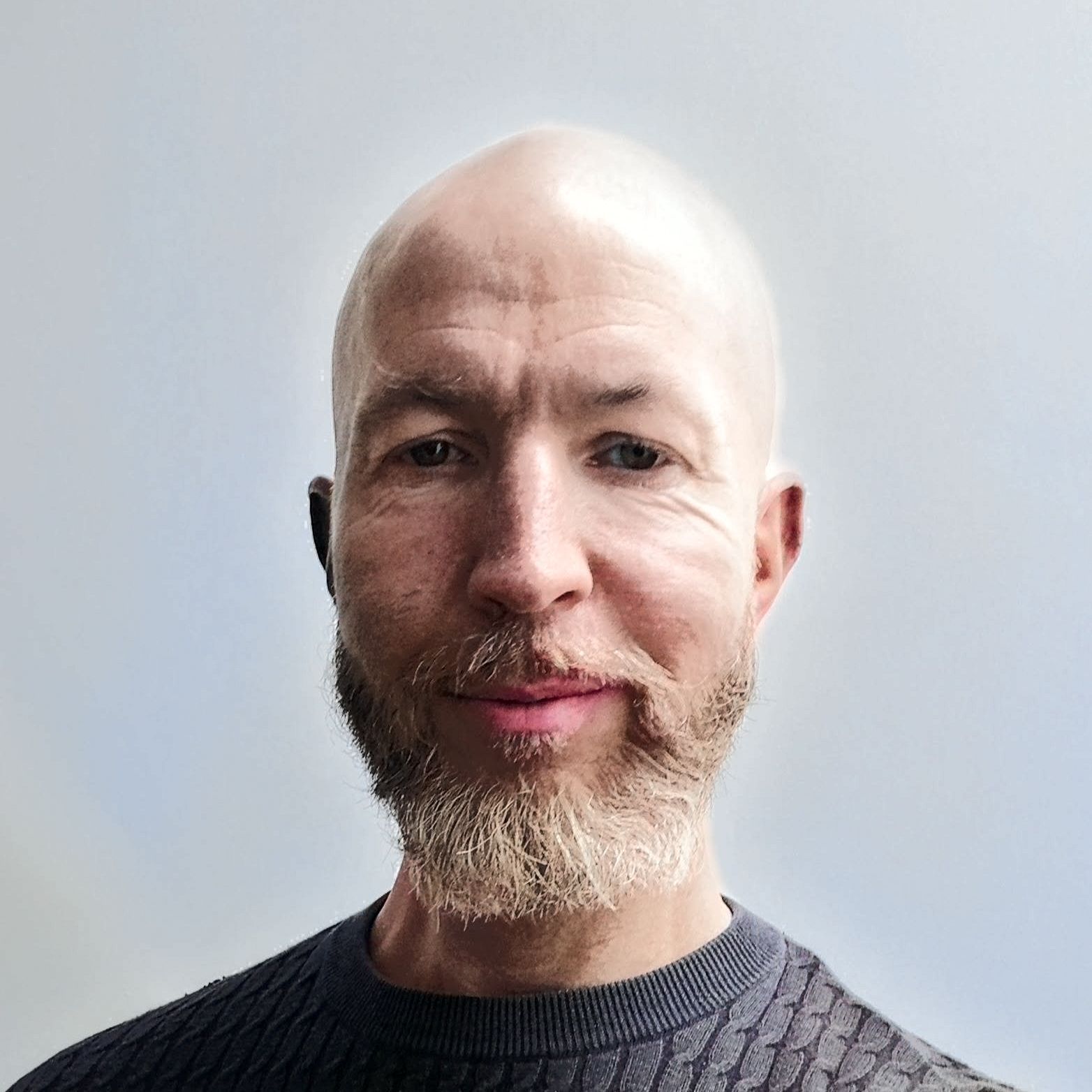 A bald man with a beard is wearing a sweater and smiling.
