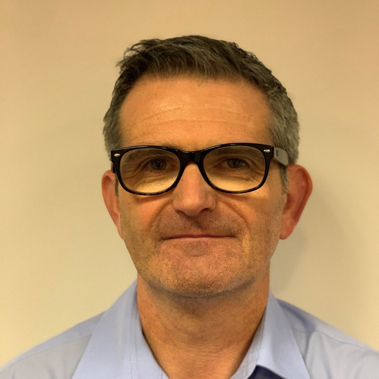 A man wearing glasses and a blue shirt looks at the camera