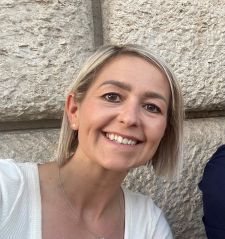 A woman in a white shirt is smiling in front of a stone wall.