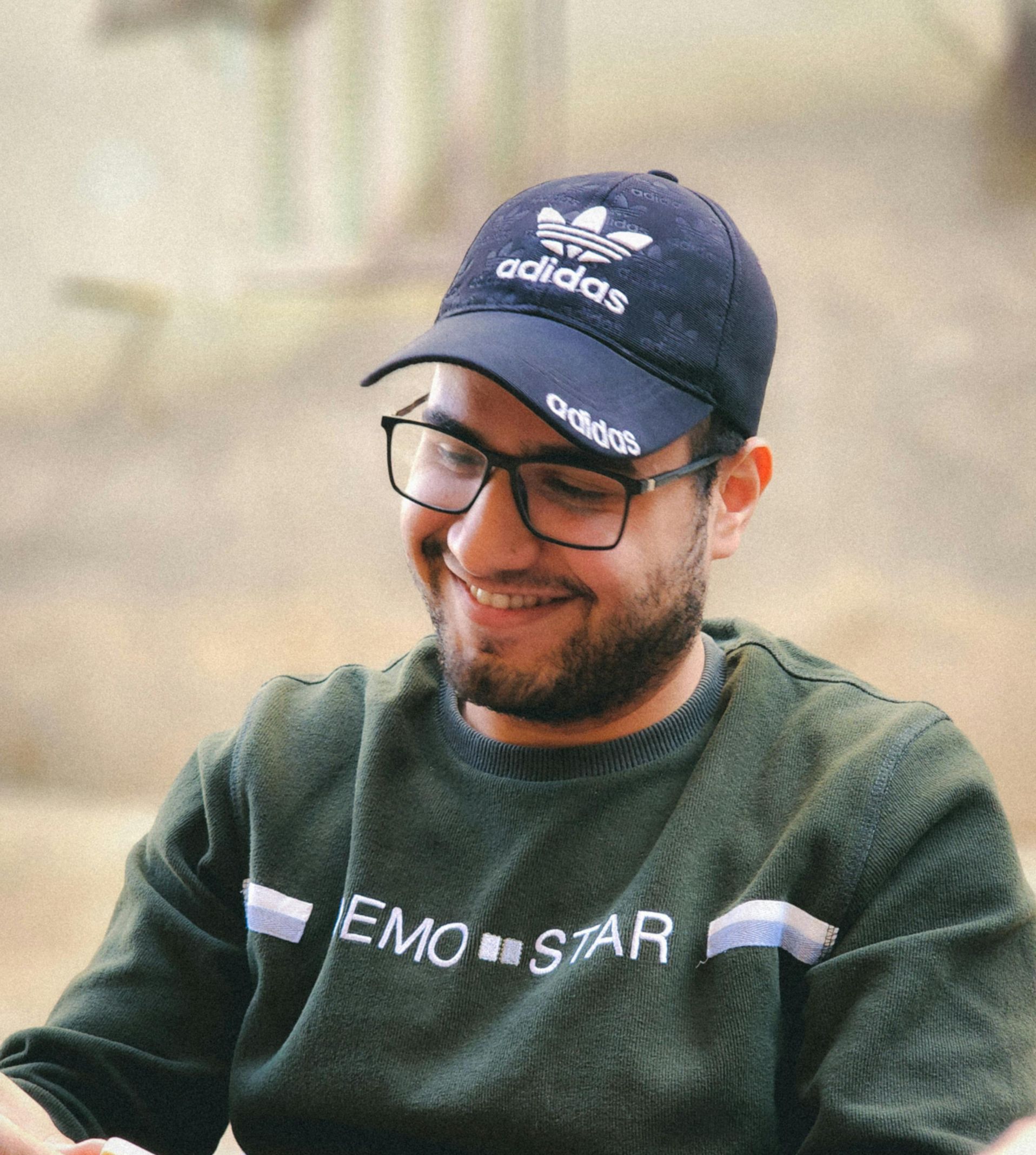 A man wearing glasses and an adidas hat is smiling