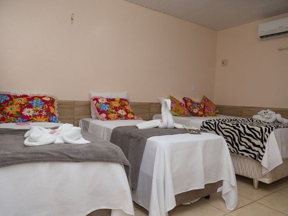 Um quarto de hotel com três camas de solteiro, cada uma com lençóis brancos, cobertores cinza e almofadas decorativas coloridas.