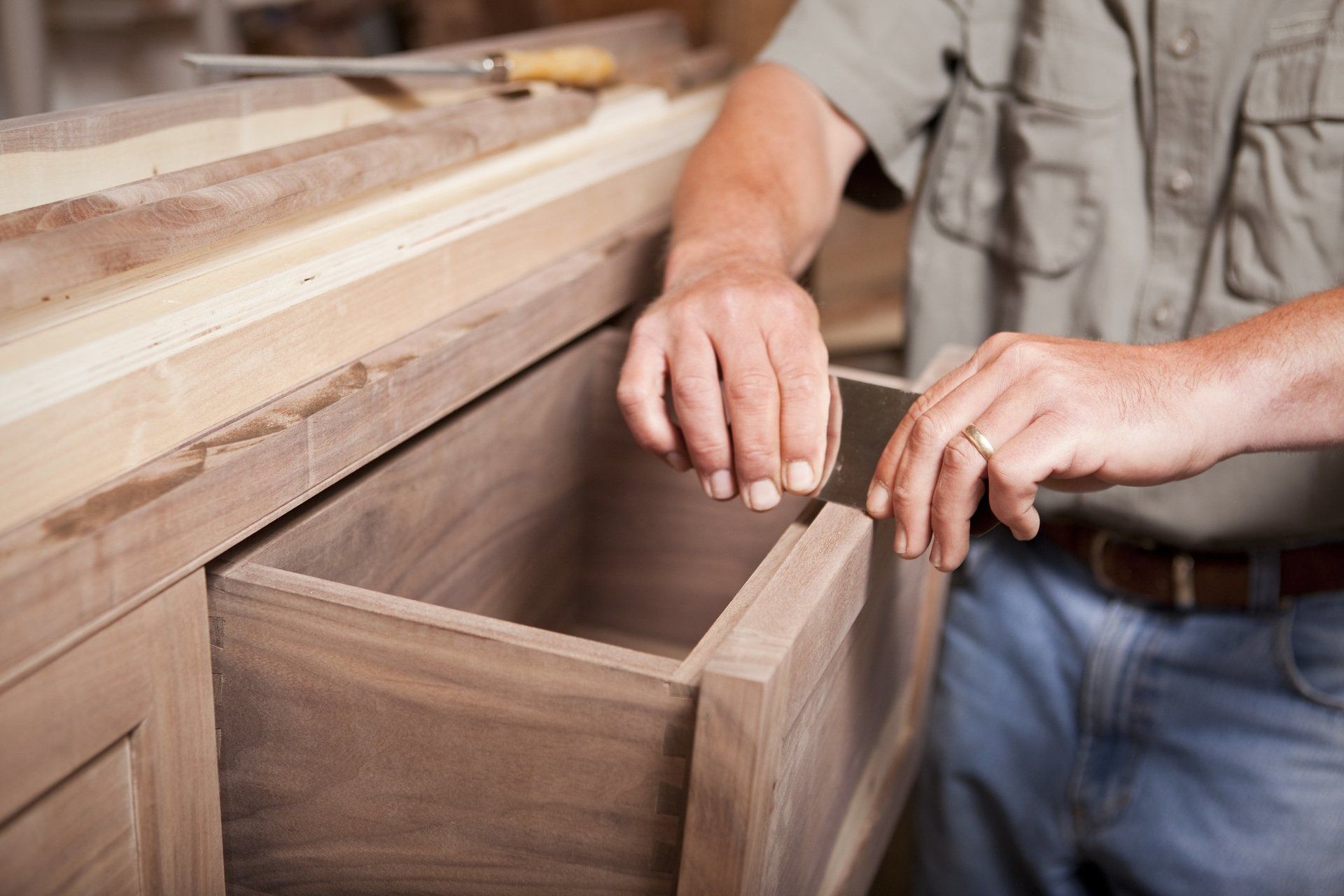 A man is opening a wooden drawer with a screwdriver.