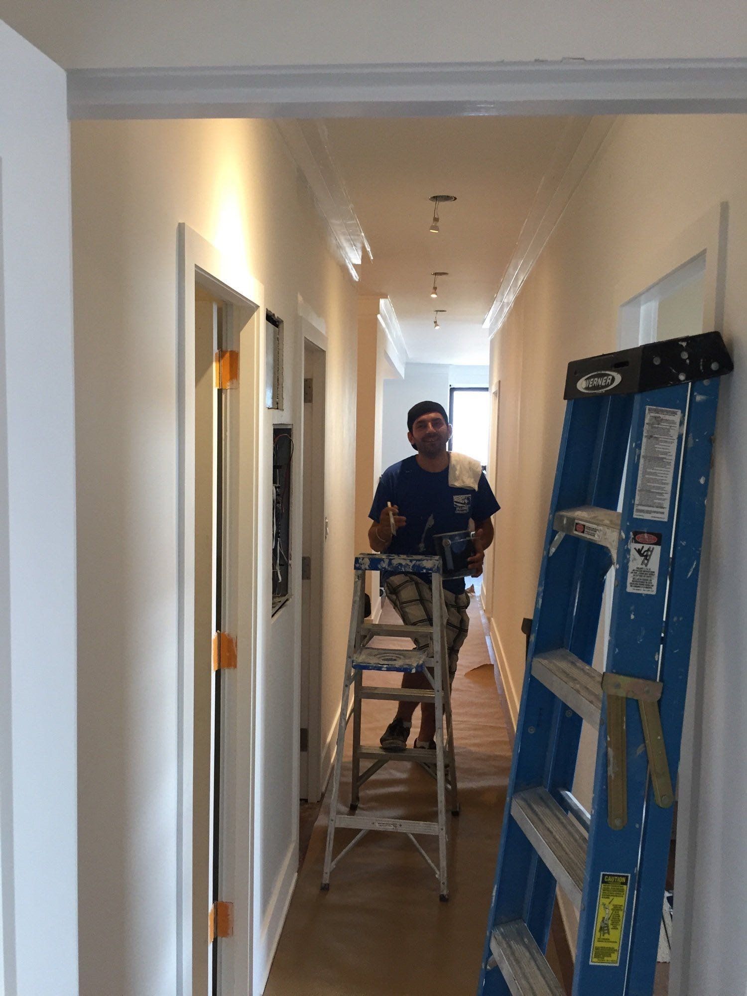 A man is sitting on a ladder in a hallway next to a blue ladder.