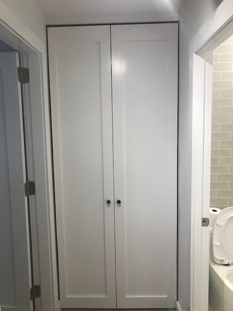 A white cabinet in a bathroom next to a toilet.