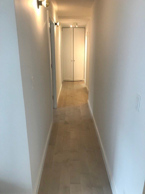 A long hallway with white walls and wooden floors in a house.