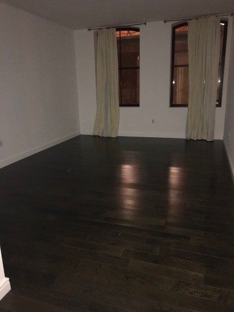 An empty living room with hardwood floors and two windows.