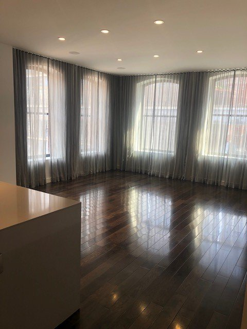 A large empty living room with hardwood floors and lots of windows.