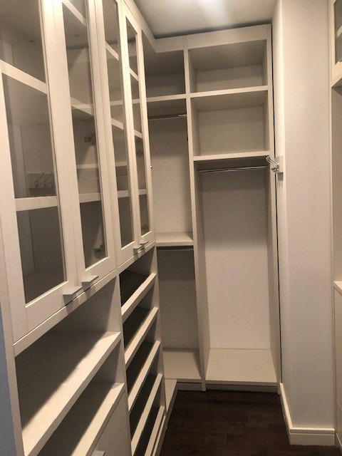 A walk in closet with white shelves and glass doors