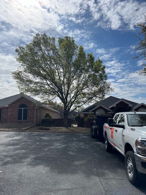 Two white trucks are parked in a driveway in front of a house.