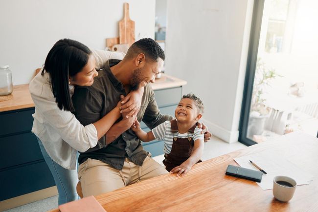Family sharing a playful moment at a bright kitchen table with coffee mugs and a phone nearby
